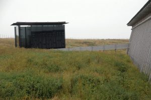 This smoked glass structure is Louise Bourgeois' part of the memorial. It's known as the House of Flames. The structure is roughly cubical, about 18 feet to a side. Once you're inside, you can look out across the sea or back to the church and the graveyard. — at Steilneset Memorial in Vardø, Norway.